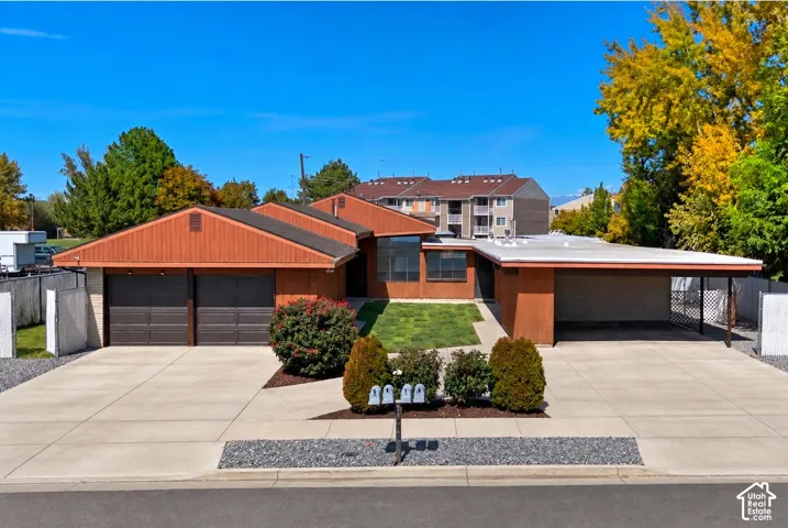 Exterior featuring wood-panel siding, a two-car garage, an attached carport, a concrete driveway, and landscaped front yard