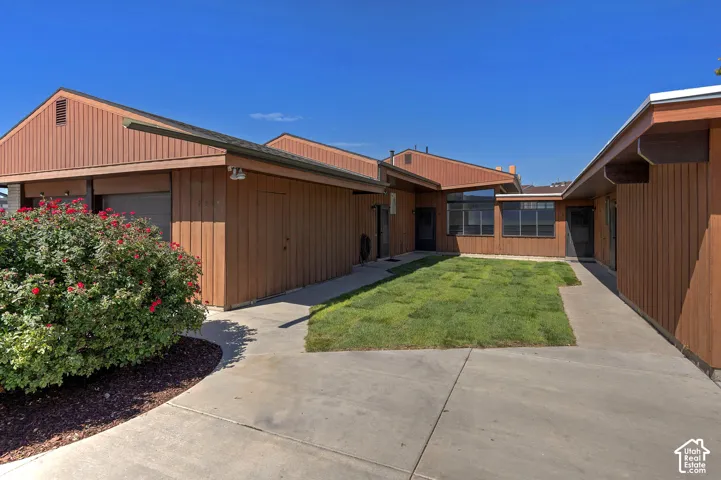 Exterior featuring wood panel siding, multiple windows, a concrete walkway, a central lawn area, and mature landscaping