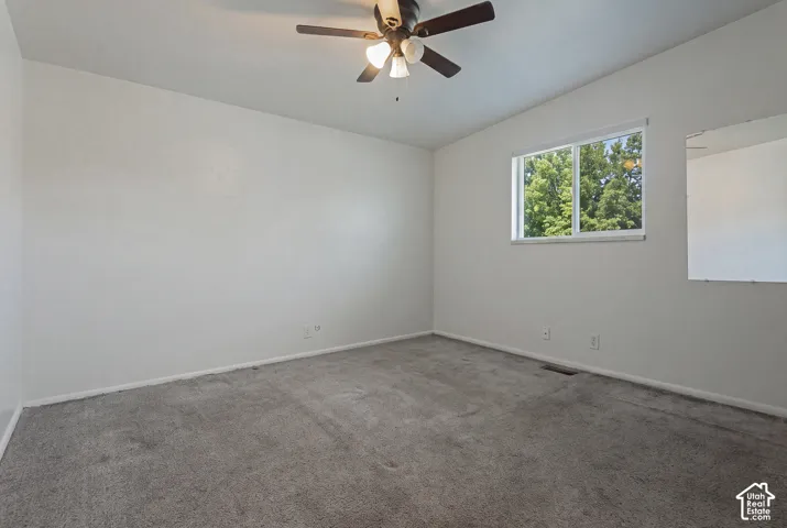 Carpeted room with a ceiling fan, white walls, and a window