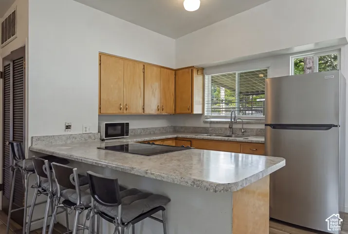 Kitchen featuring wood cabinetry, stone-finish countertops, stainless steel refrigerator, and integrated cooktop