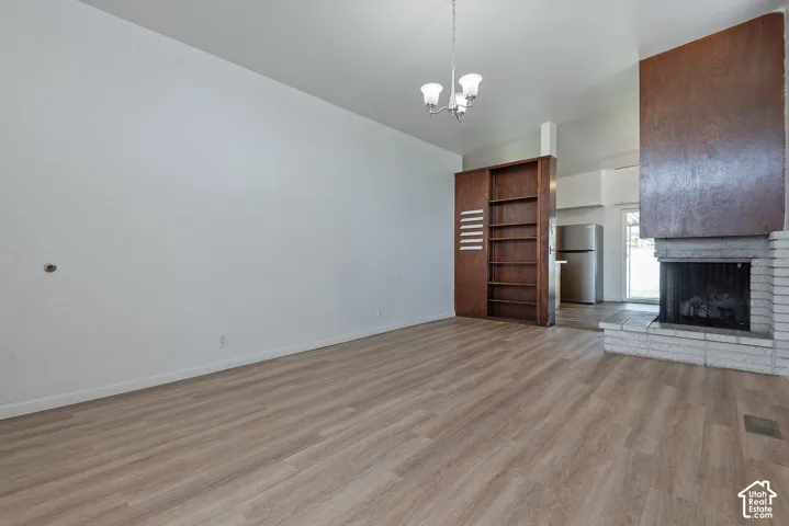 Wood-finish flooring throughout, prominent brick fireplace with wood-paneled surround, built-in shelving, and a suspended chandelier
