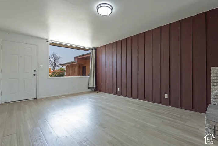 Wood-finish flooring, accent wall with vertical paneling, white door with black hardware, and a built-in stone feature