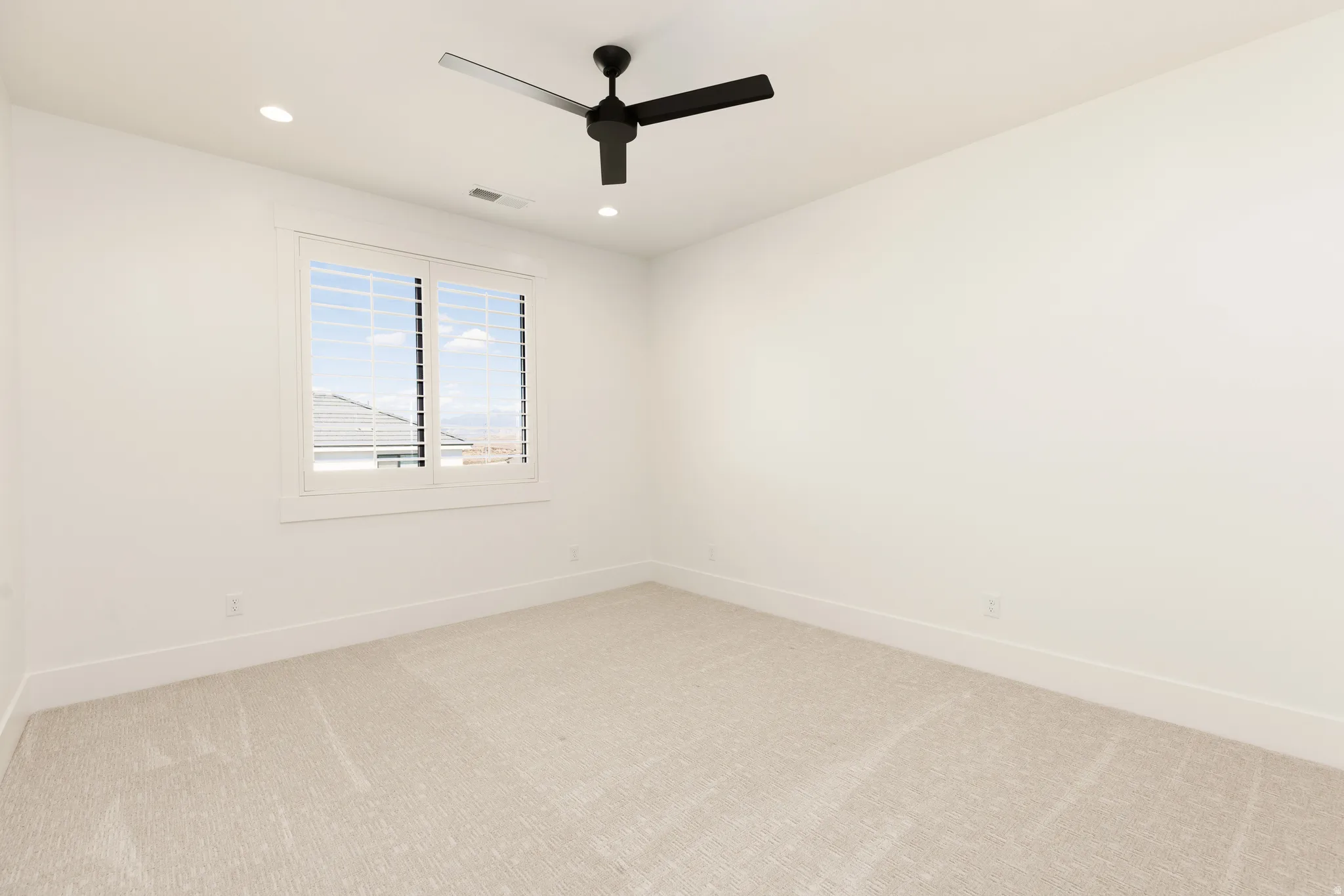 Light-colored carpeted flooring, white walls, and a window with white louvered shutters