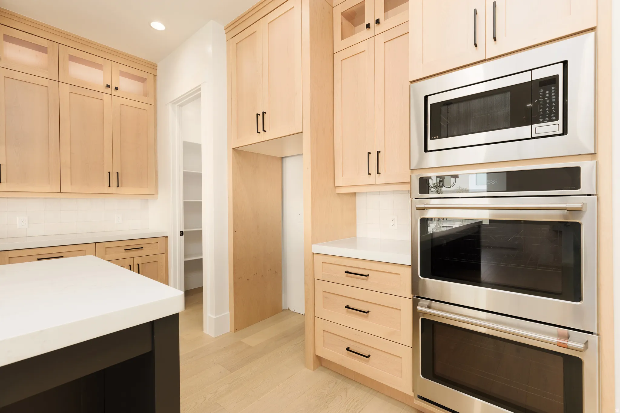 Light wood-finish cabinetry, stainless steel built-in appliances, white countertops, and wood-finish flooring