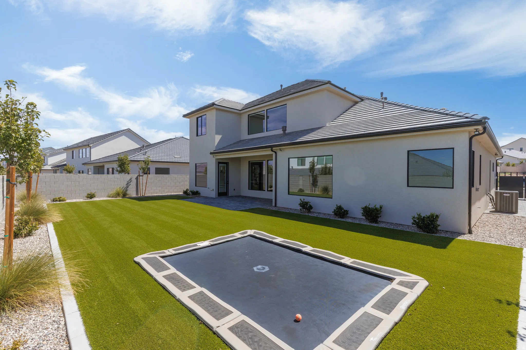 Backyard featuring an in-ground trampoline, artificial turf, and a paver patio