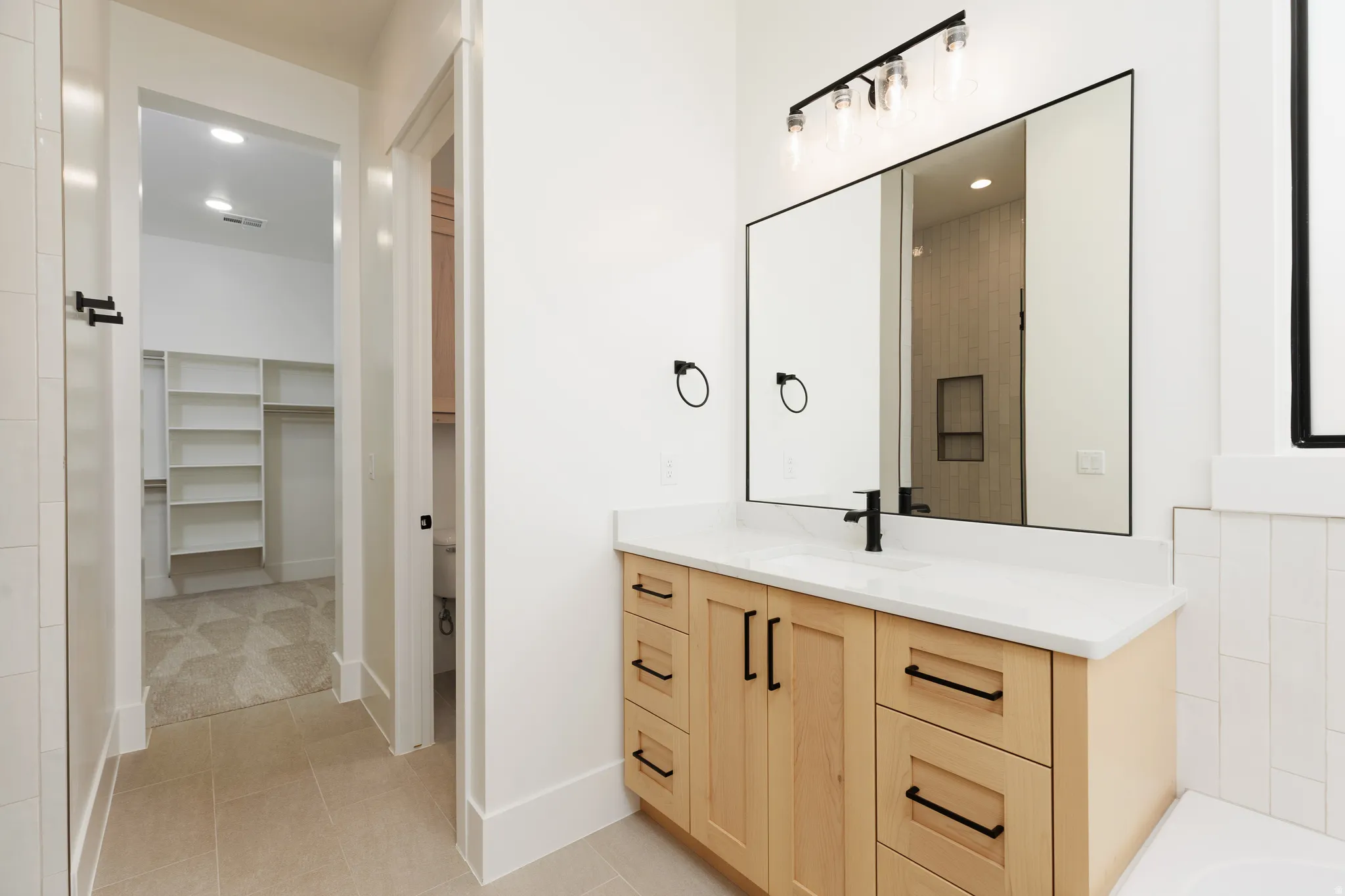 Vanity with light wood-finish cabinetry, white countertop, and matte black hardware