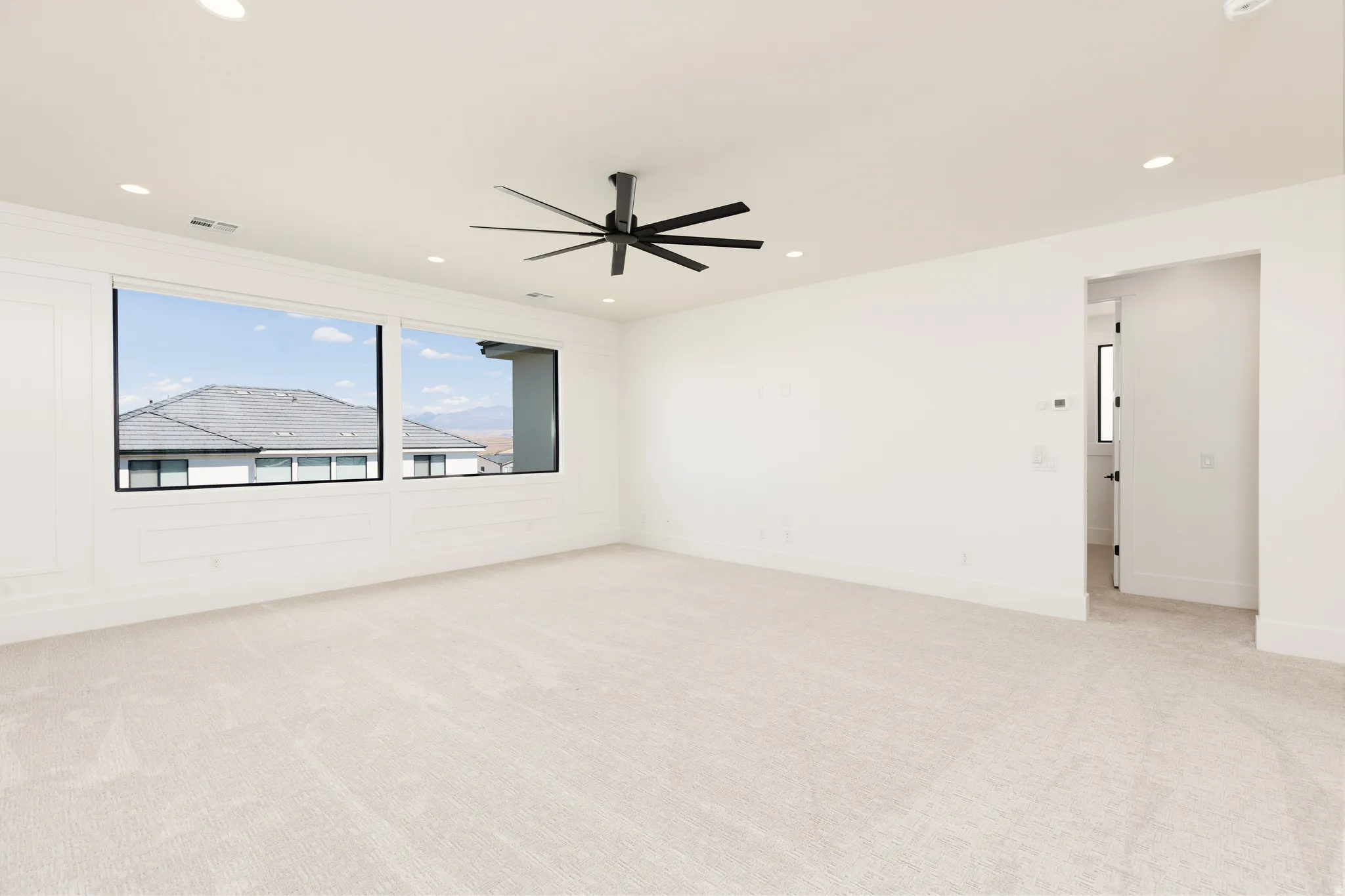 Spacious room featuring broad windows with black frames, recessed lighting, a modern black ceiling fan, and light-colored carpeting