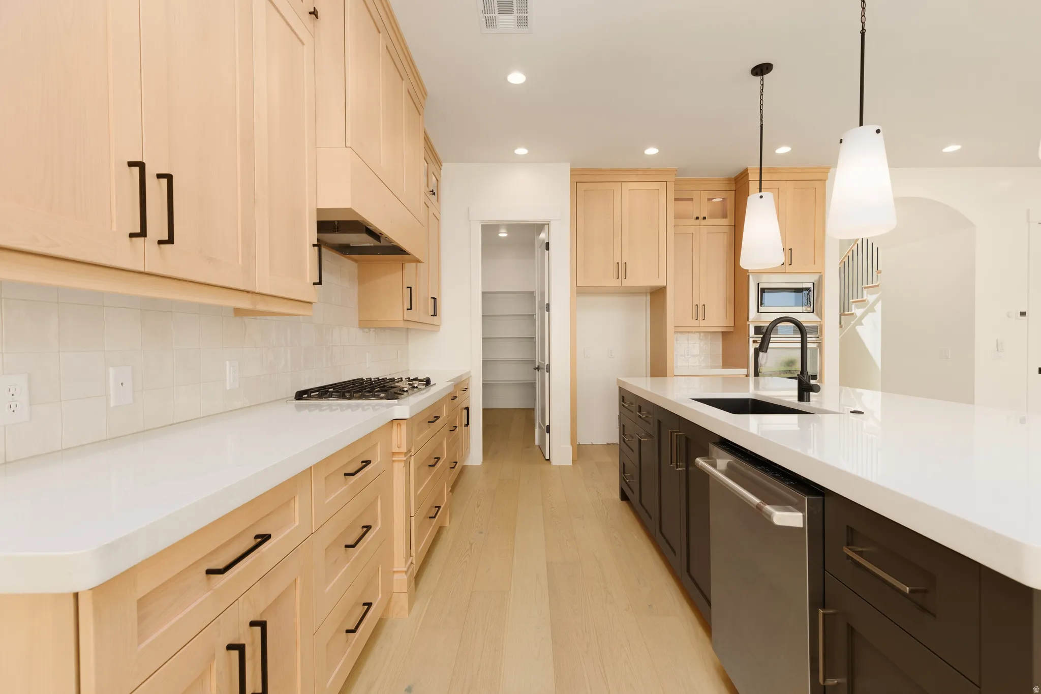 Wood-finish flooring, light-toned cabinetry, white countertops, built-in cooktop, and large kitchen island with integrated sink