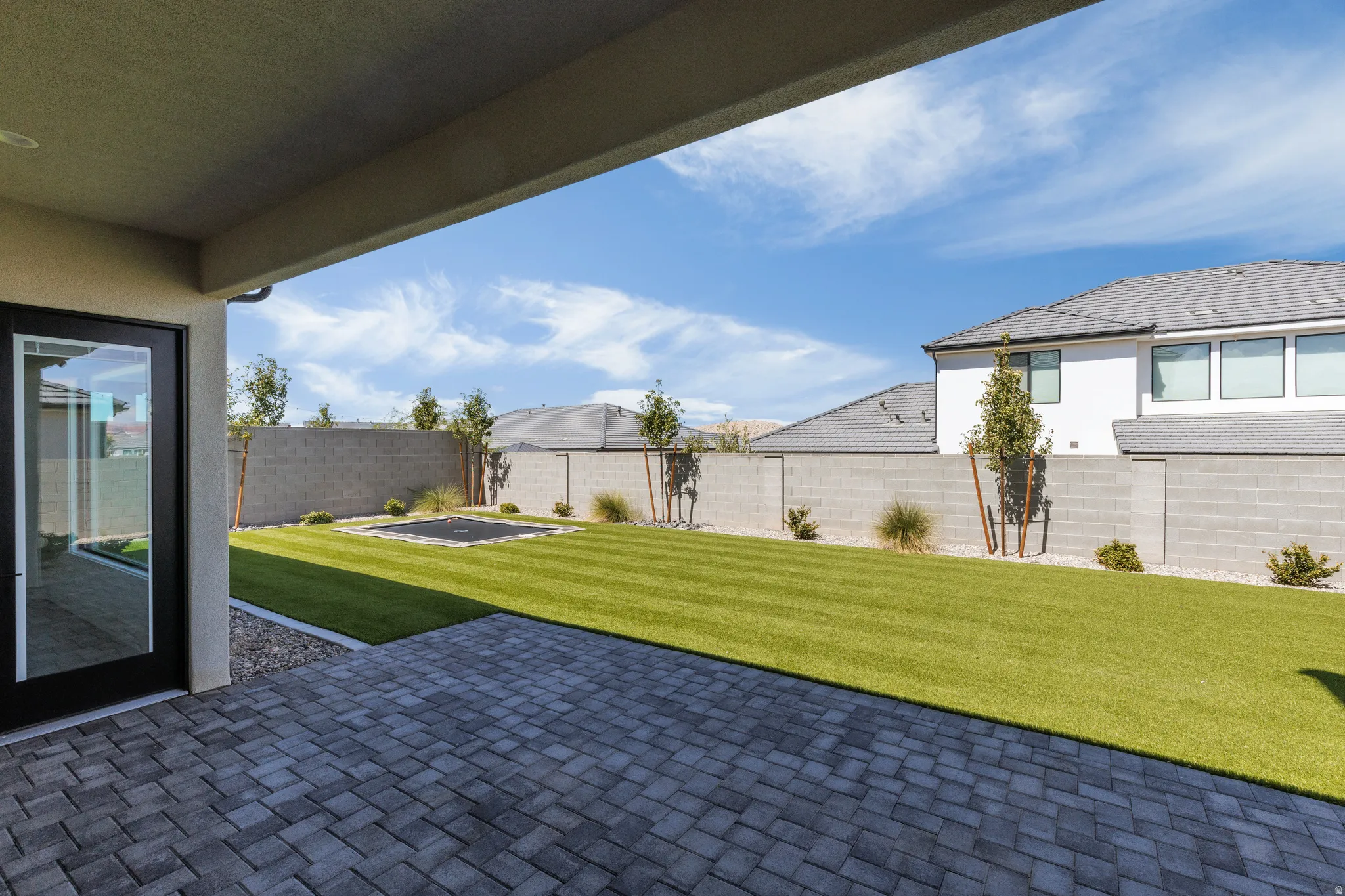 Expansive paver patio with a covered outdoor area, leading to a large manicured lawn, surrounded by a block perimeter wall