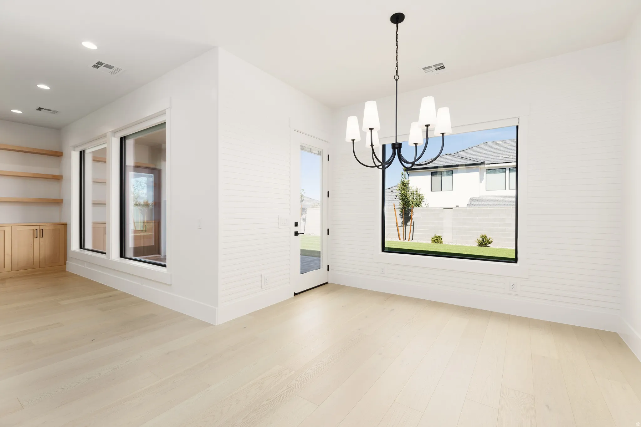 Light wood-finish flooring, built-in shelving, recessed ceiling lighting, and a contemporary chandelier