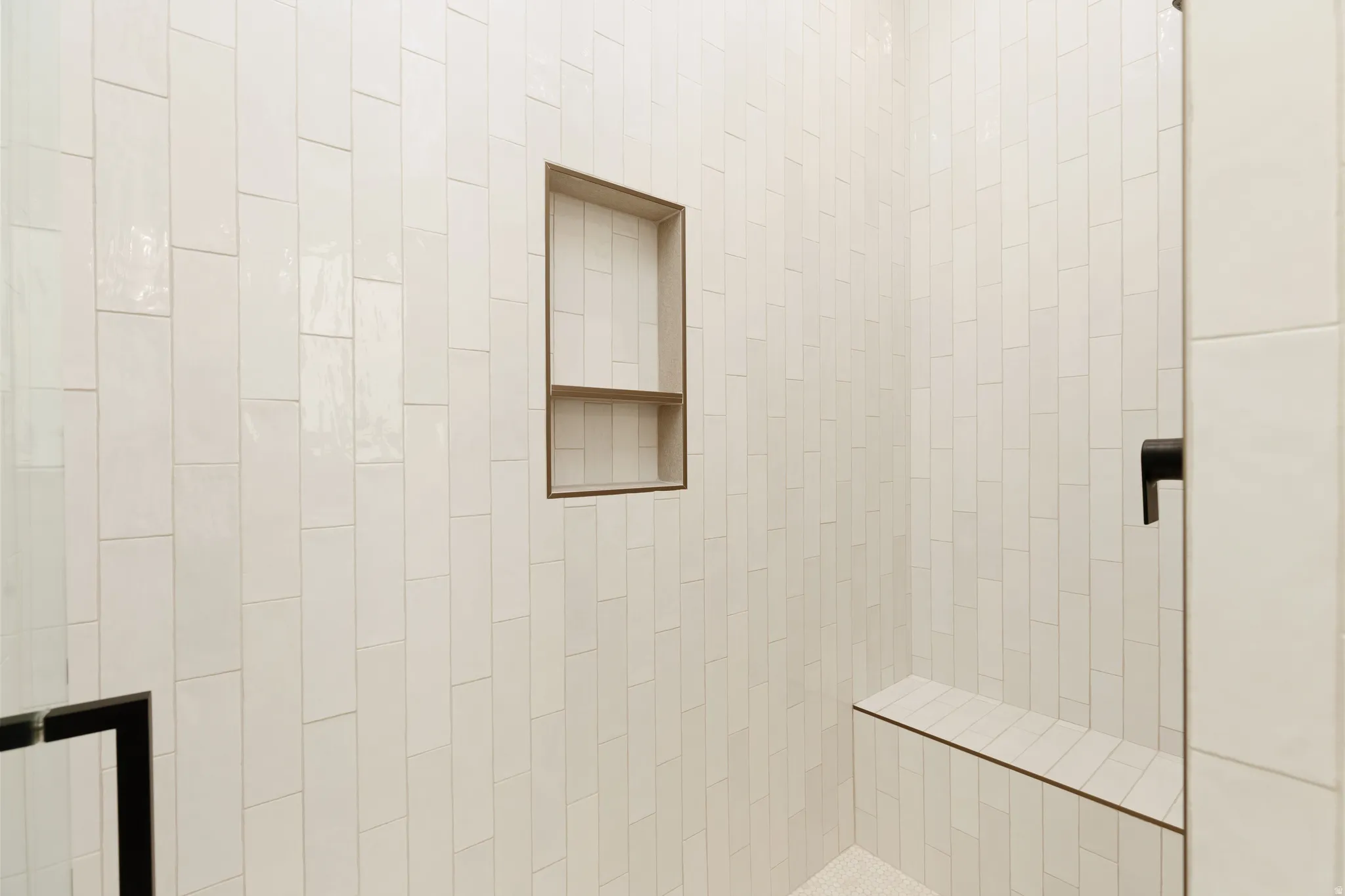 Shower enclosure featuring white vertical subway tile, built-in recessed niche, integrated bench, and dark-finish fixtures