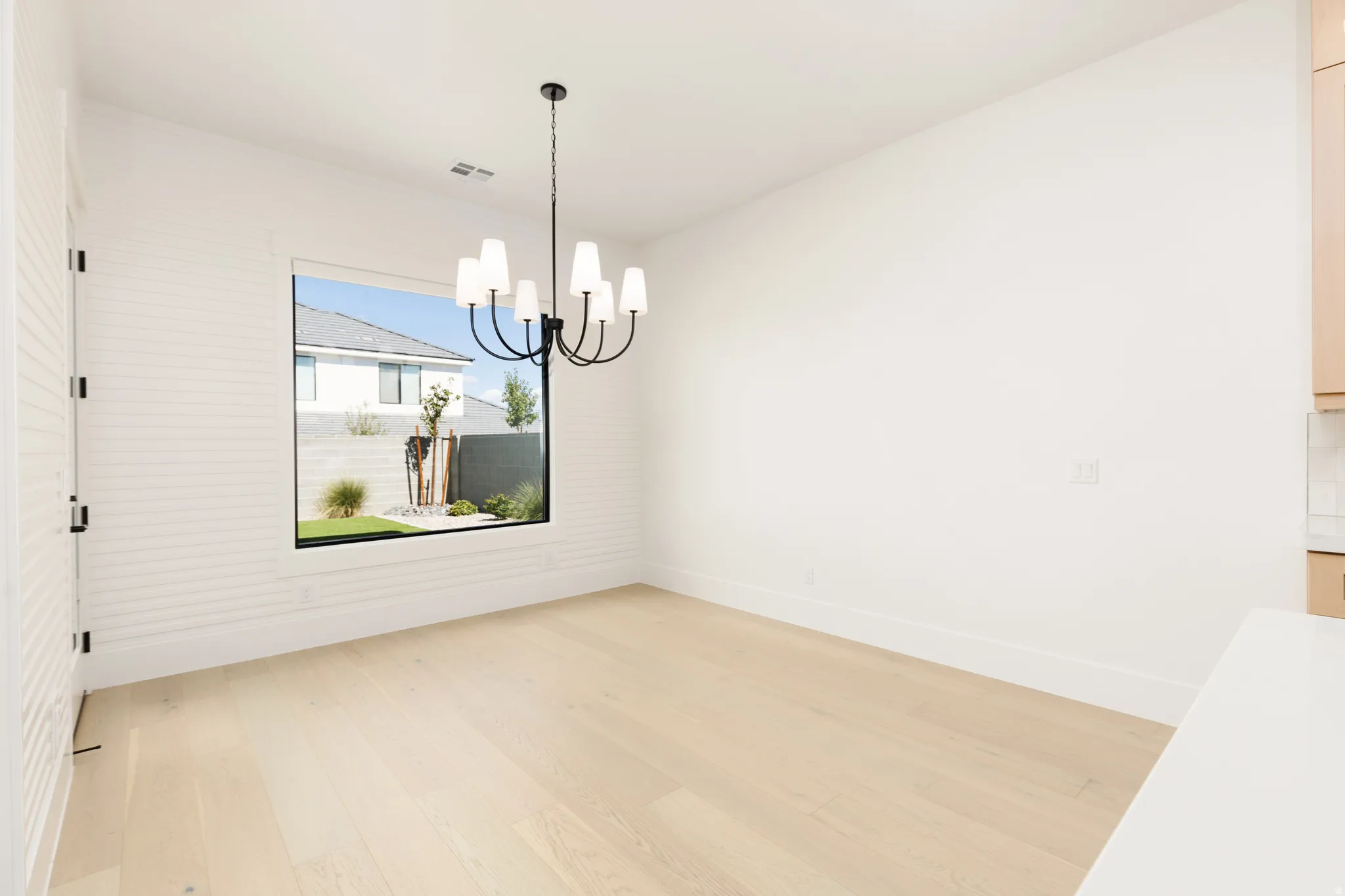 Wood-finish flooring, accent wall with horizontal paneling, black metal chandelier, large picture window