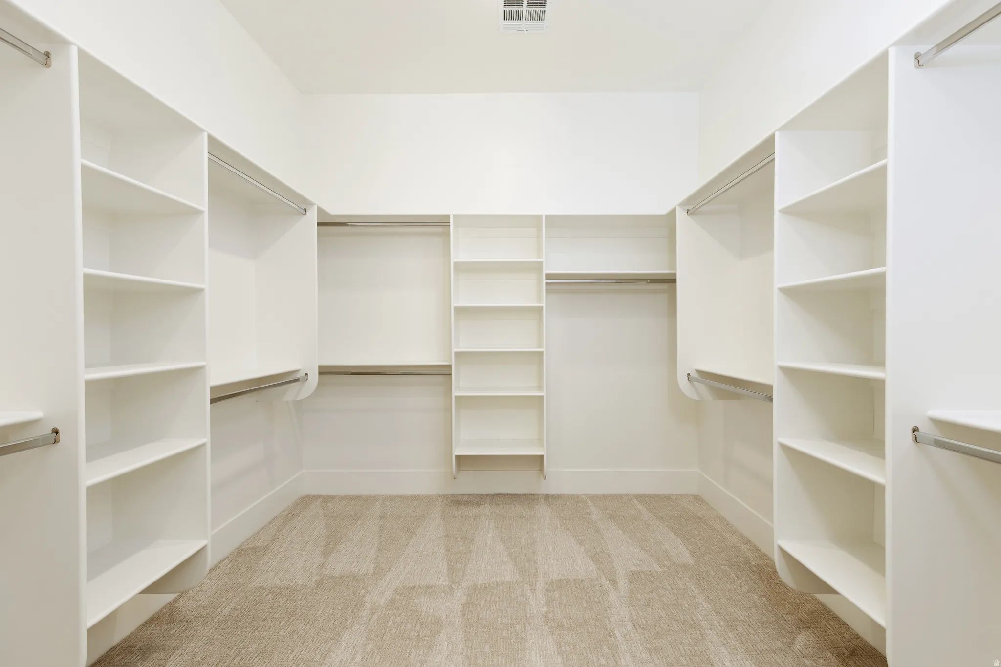 Spacious walk-in closet featuring built-in shelving, multiple hanging rods, and neutral-toned carpeting