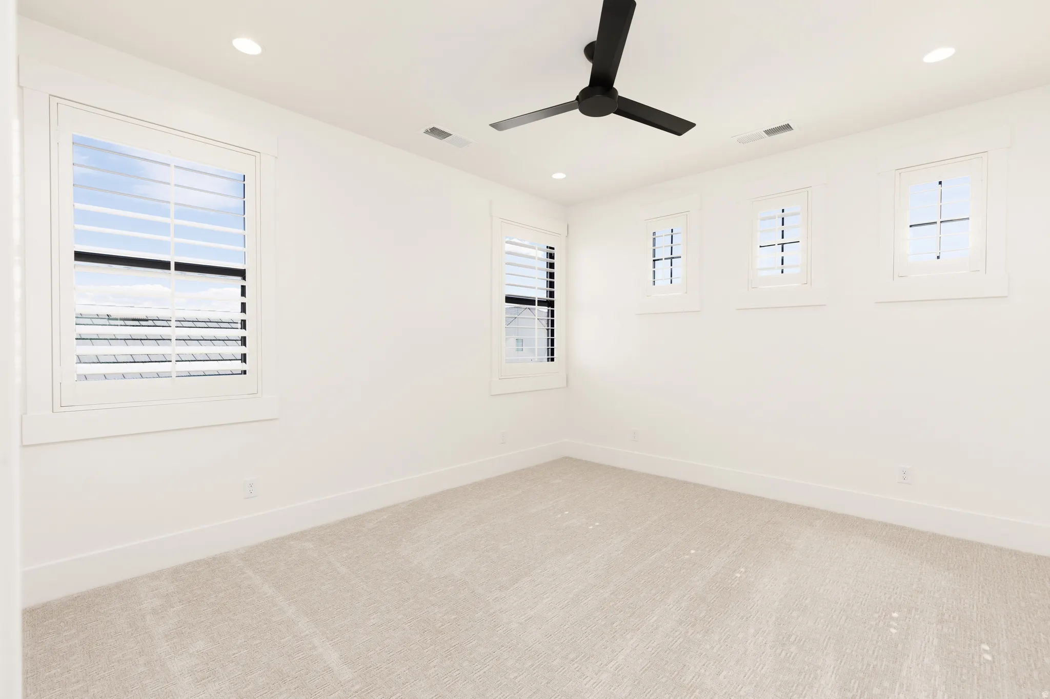 Recessed lighting, ceiling fan, multiple windows with plantation shutters, and light-toned carpeting