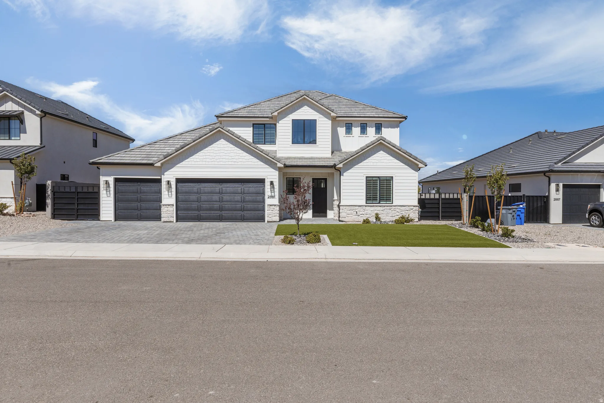 Two-story residence featuring white siding, stone accents, a gray tile roof, a two-car garage with black doors, and a paver driveway