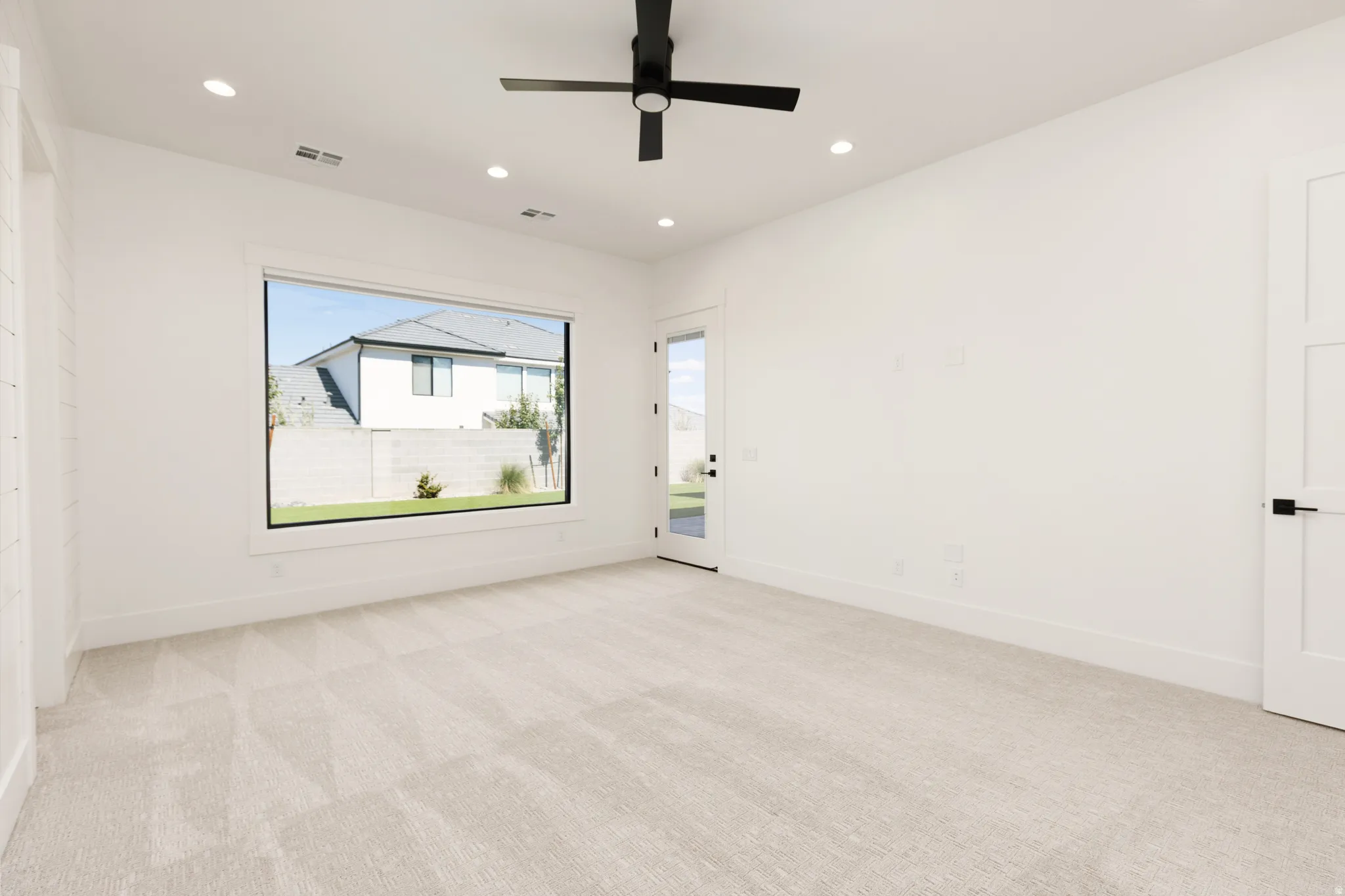 Recessed lighting, ceiling fan, expansive window, white walls, and light-toned carpeting
