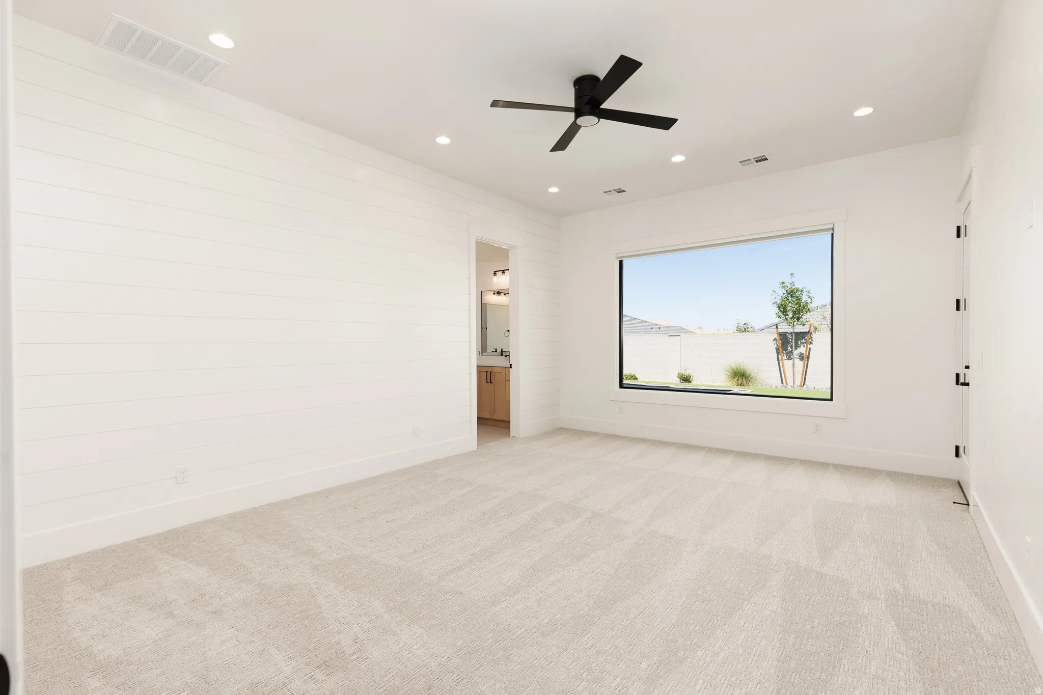 Recessed lighting, ceiling fan with matte black finish, large window, shiplap accent wall, and light-toned carpeting