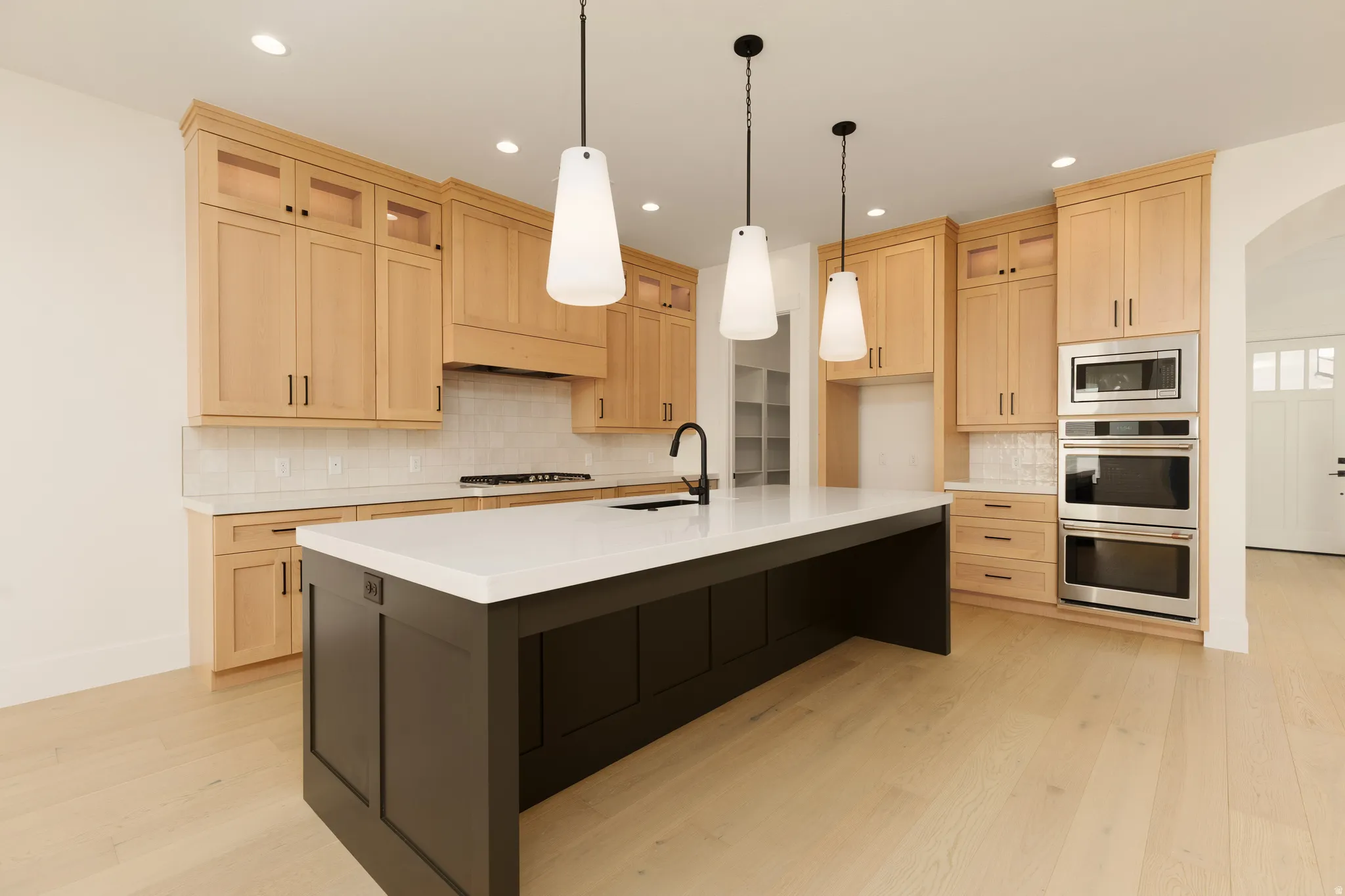 Spacious kitchen with a central dark-toned island, light wood cabinetry, recessed lighting, and integrated stainless steel appliances