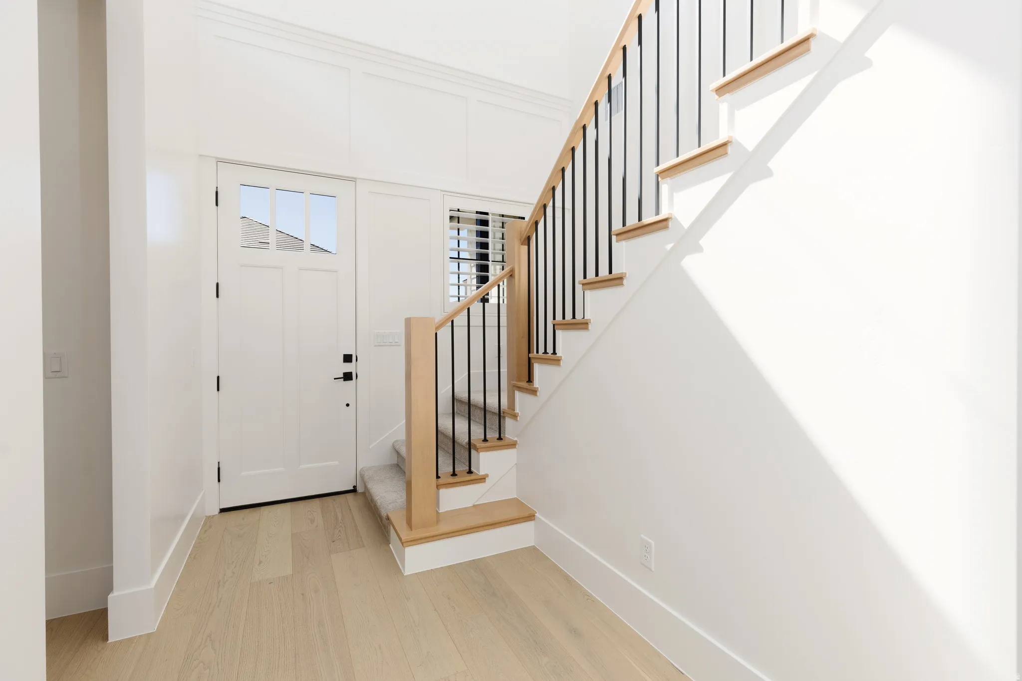 Entryway featuring light wood-finish flooring, a contemporary staircase with iron balusters, and a white paneled door with upper glass inserts
