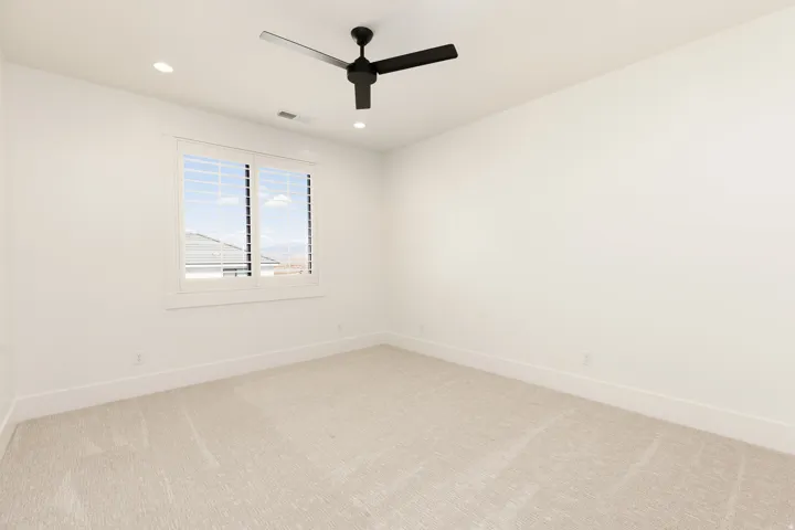 Light-colored carpeted flooring, white walls, and a window with white louvered shutters