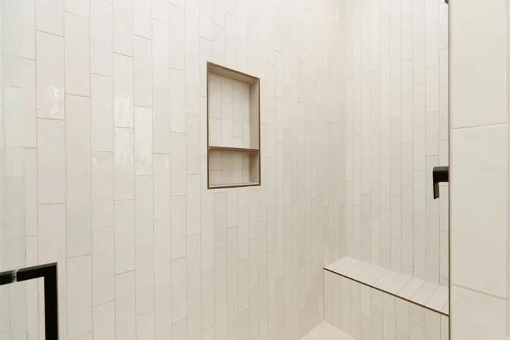 Shower enclosure featuring white vertical subway tile, built-in recessed niche, integrated bench, and dark-finish fixtures