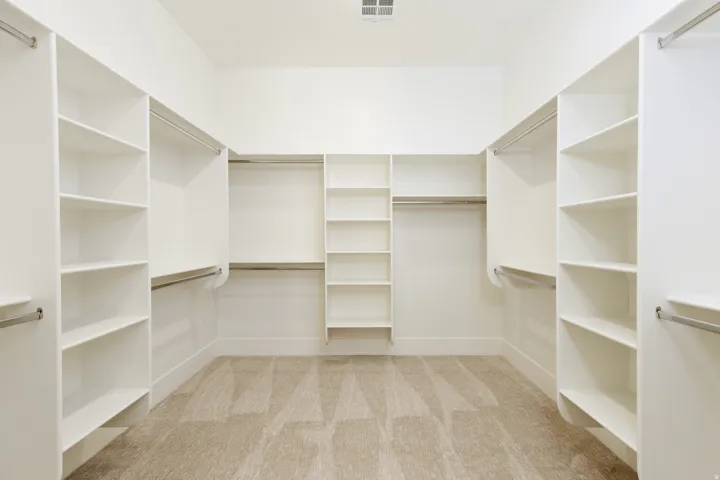 Spacious walk-in closet featuring built-in shelving, multiple hanging rods, and neutral-toned carpeting
