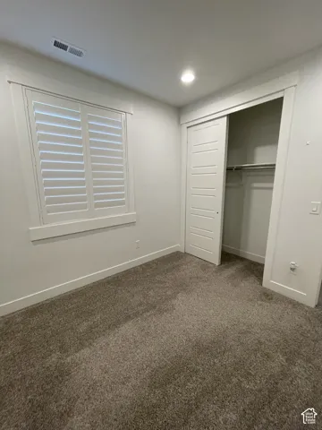 Plush carpeting, recessed ceiling lighting, and a window with plantation shutters