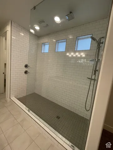 Walk-in shower with subway tile surround, clear glass enclosure, multiple showerheads, and recessed ceiling lighting