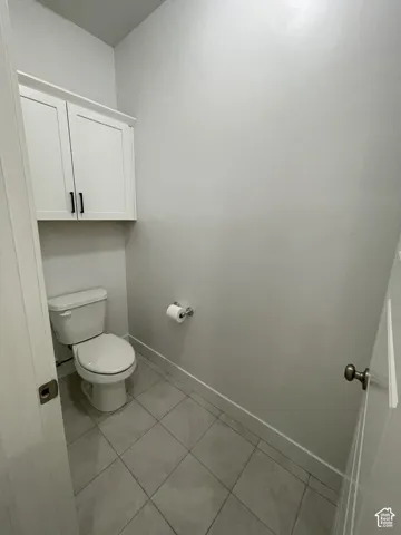 White cabinetry with dark hardware, white toilet, and gray tile flooring