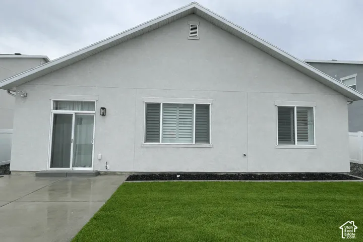 Rear exterior featuring a sliding glass door, two windows with horizontal blinds, and a concrete patio