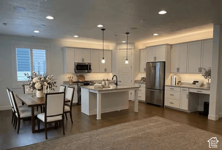 Spacious open-concept layout featuring recessed lighting, wood-finish flooring, white shaker cabinetry, stainless steel appliances, and a central kitchen island with a dark faucet