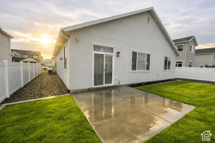 Stucco exterior with a pitched roofline, featuring a concrete patio, sliding glass door, and a white vinyl fence