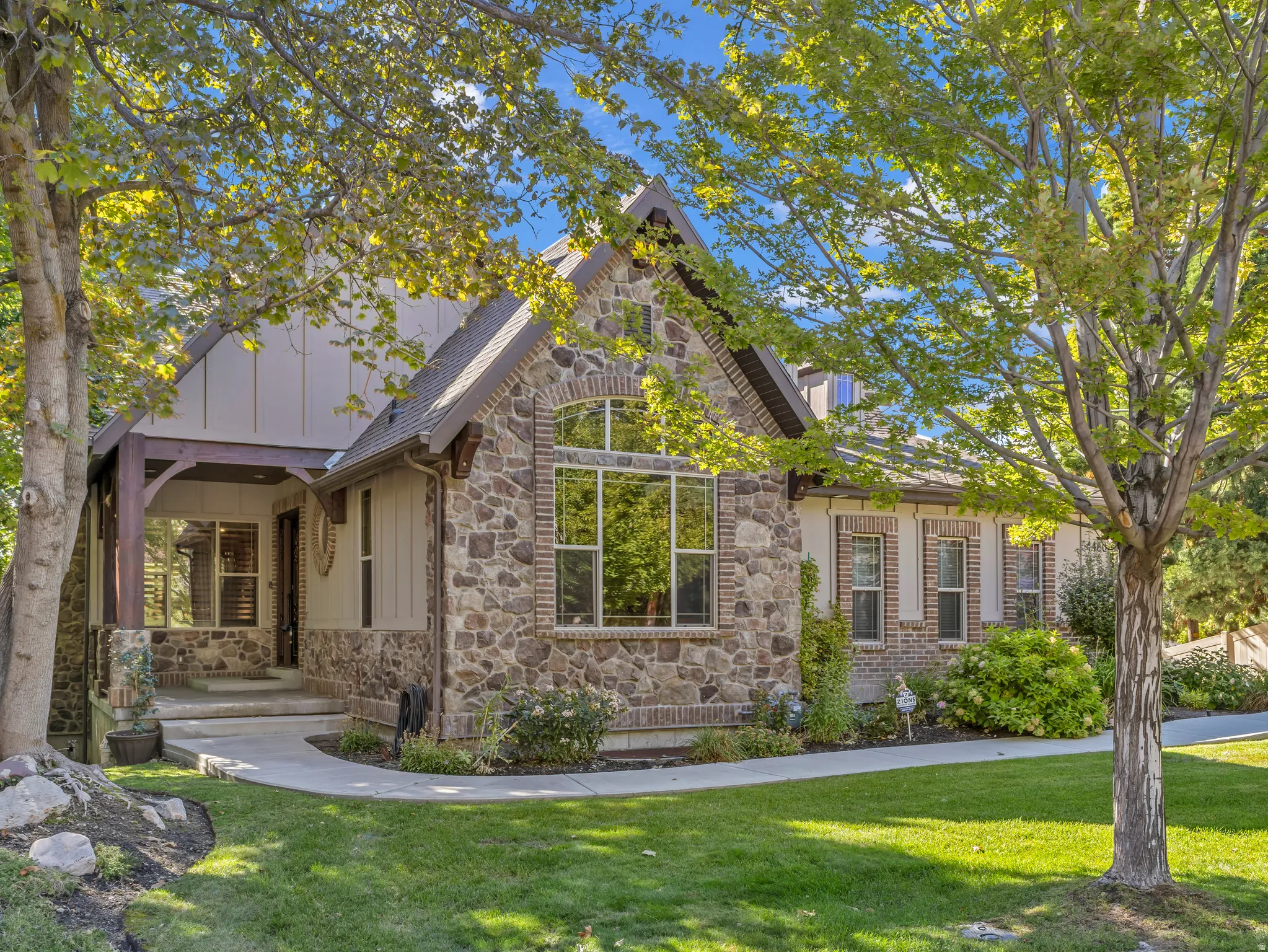 Stone and brick exterior with arched windows, gabled roofline, covered entry, and manicured lawn
