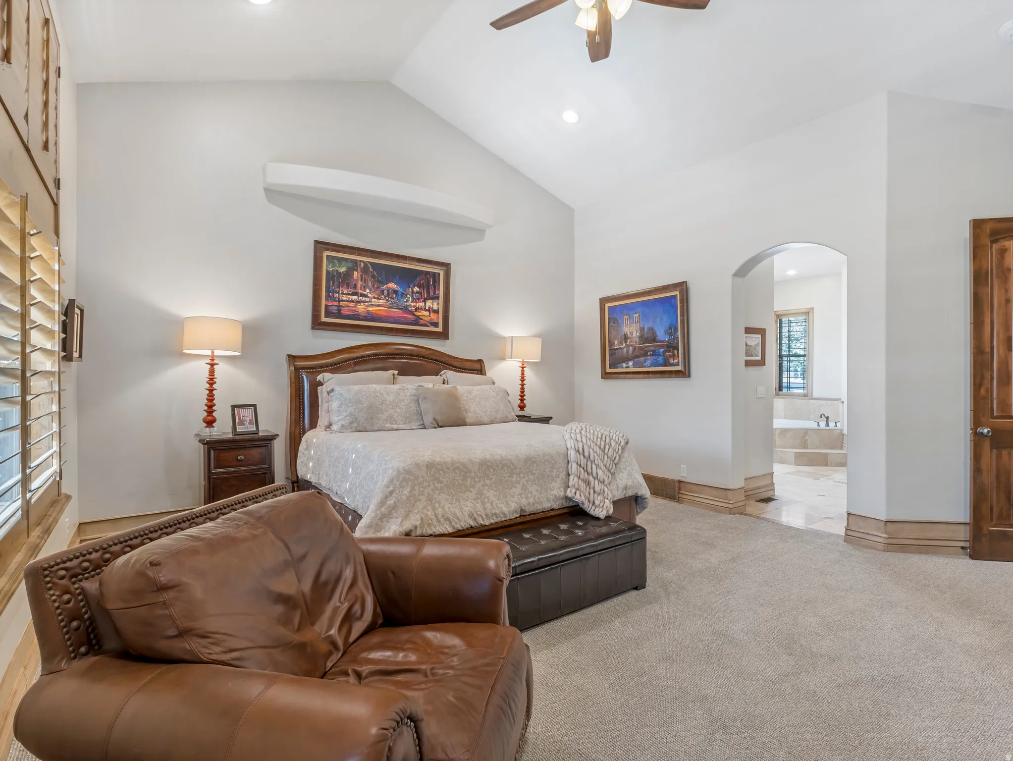 Vaulted ceiling with a ceiling fan, wood-shutter window treatments, and an arched entry to an adjacent room