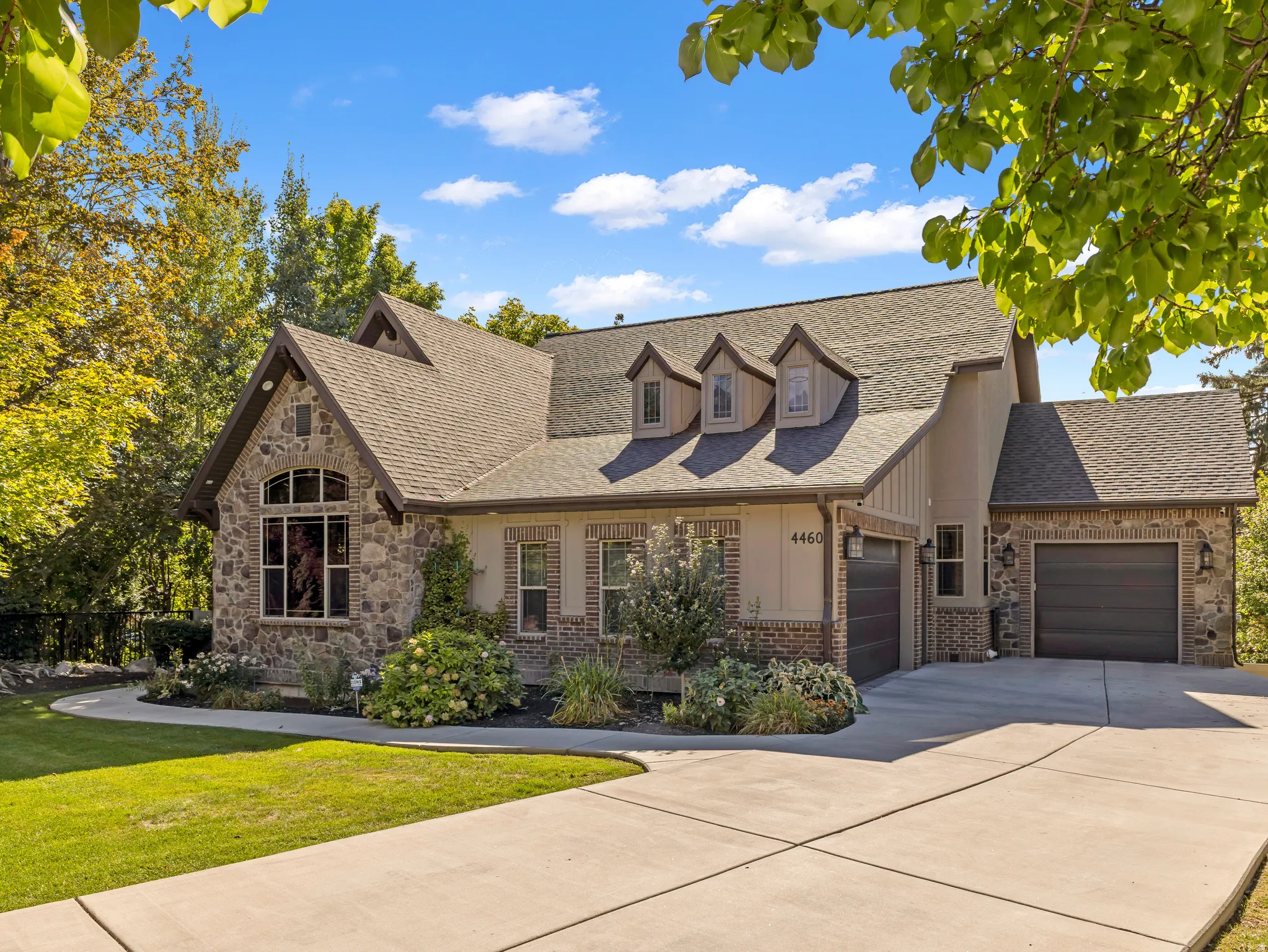 Stone and brick veneer exterior with an arched window, multiple gabled dormers, an attached two-car garage, and a concrete driveway