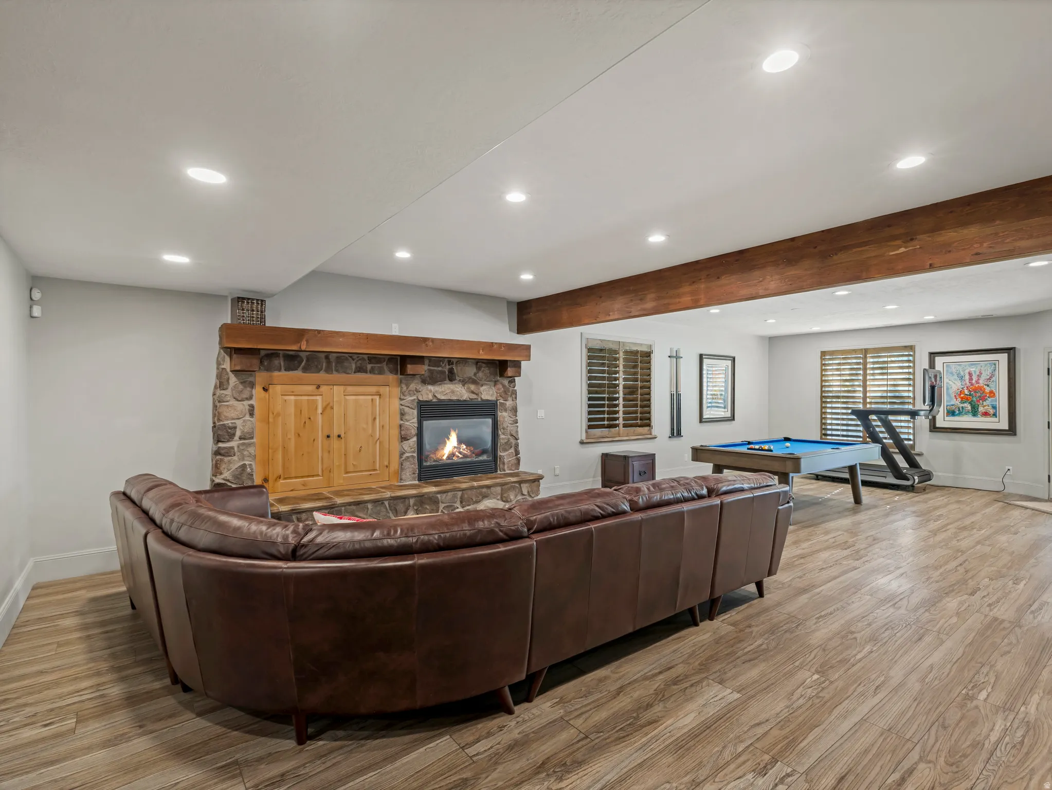Stone fireplace with wood mantel, built-in cabinetry, wood-finish flooring, and exposed ceiling beams