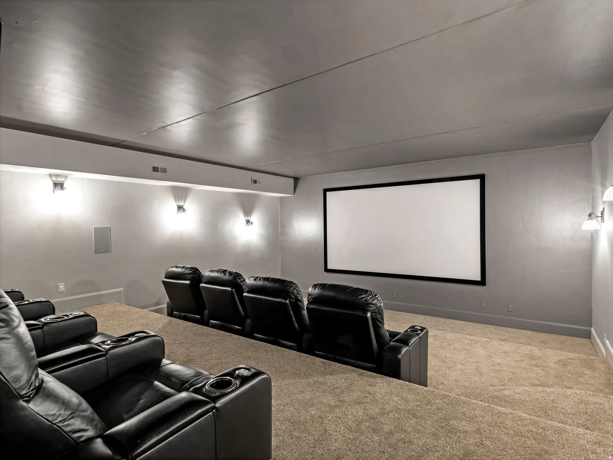 Dedicated media room with tiered carpeted flooring, large projection screen, and wall-mounted sconce lighting