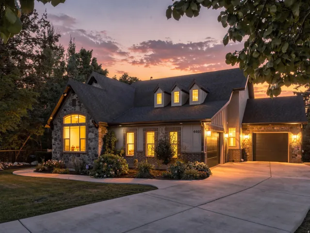 Stone and stucco exterior featuring a multi-gabled roofline, dormer windows, and attached garages