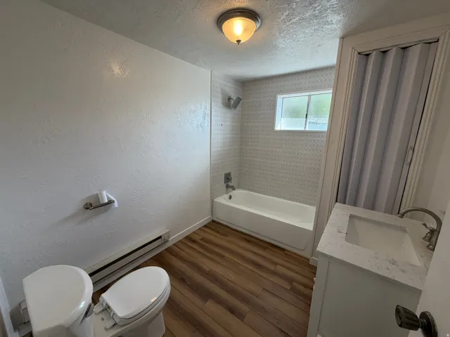 Bathroom featuring a white vanity with an integrated sink, wood-finish flooring, and a bathtub with tiled surround