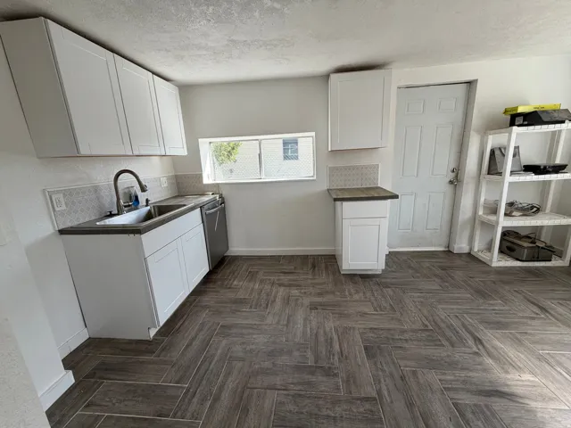 Herringbone-pattern wood-finish flooring, white shaker-style cabinetry, stainless steel double-basin sink, and a patterned backsplash