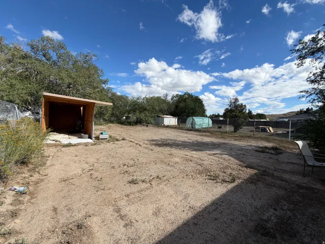 Open-air shed with a sloped roof and concrete pad, surrounded by mature trees and a fenced area