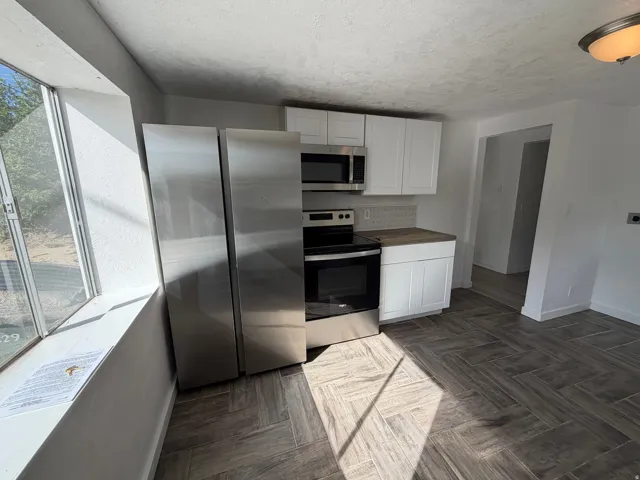Stainless steel appliances, white cabinetry, wood-finish countertops, tile backsplash, and wood-finish flooring in a herringbone pattern