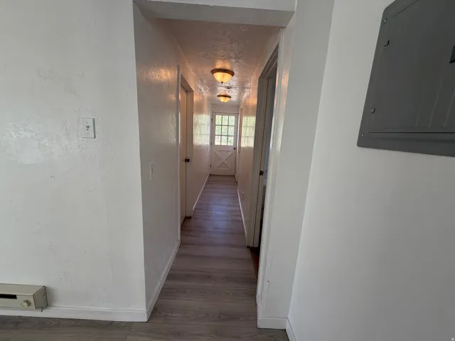 Hallway featuring wood-finish flooring, two flush-mount light fixtures, and a white paneled door with glass inserts