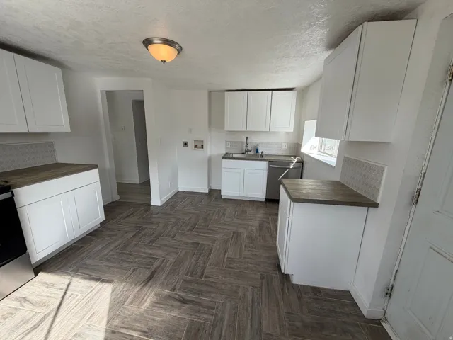 Kitchen featuring white shaker-style cabinetry, wood-finish countertops, geometric tile backsplash, and herringbone-patterned flooring