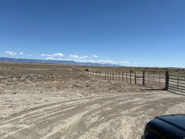 Expansive open terrain with a long fence line, multiple gates, and distant mountains