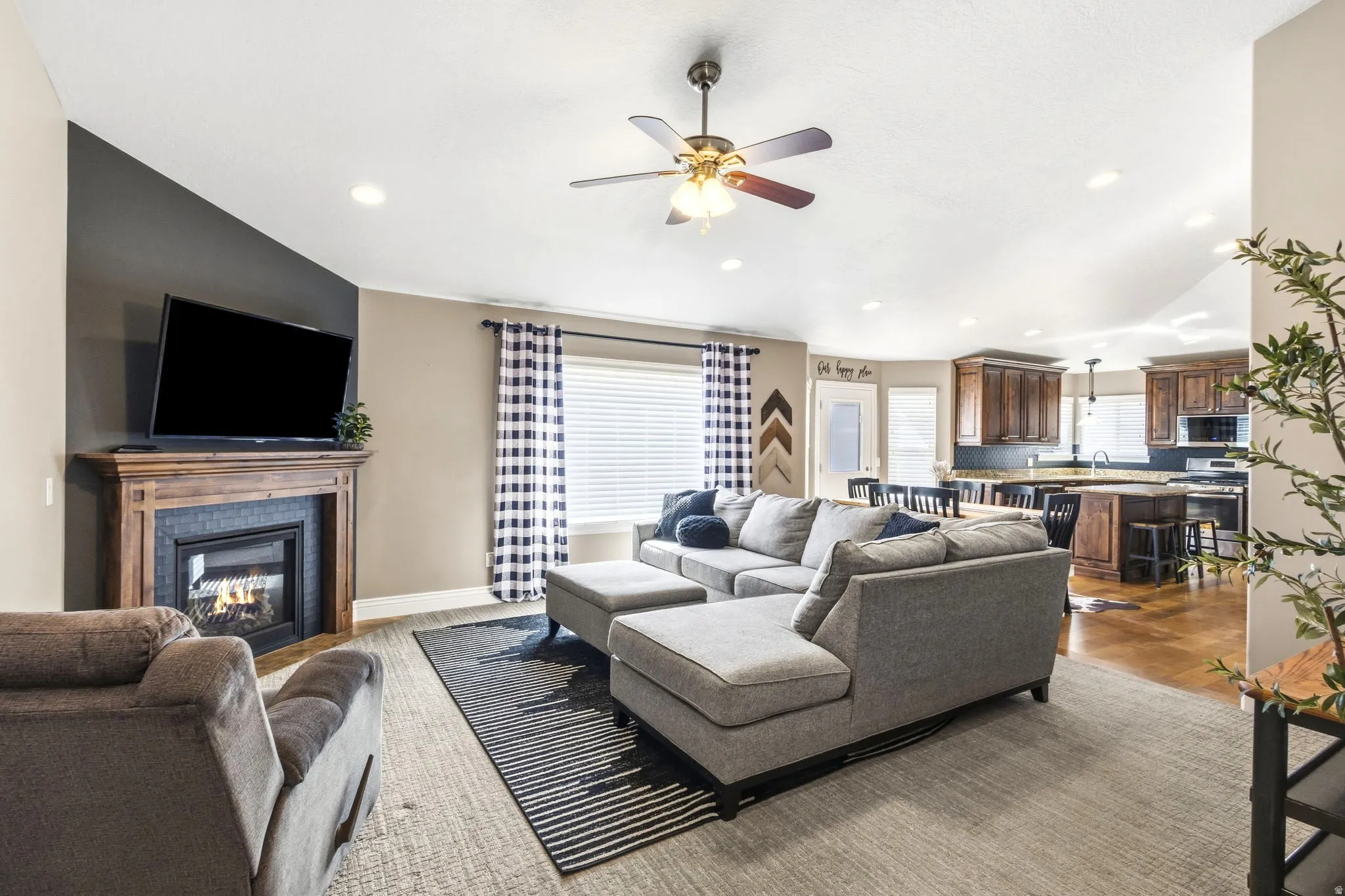 Open-concept living space featuring a fireplace with a wood mantel, recessed lighting, ceiling fan, and hardwood flooring in the kitchen area