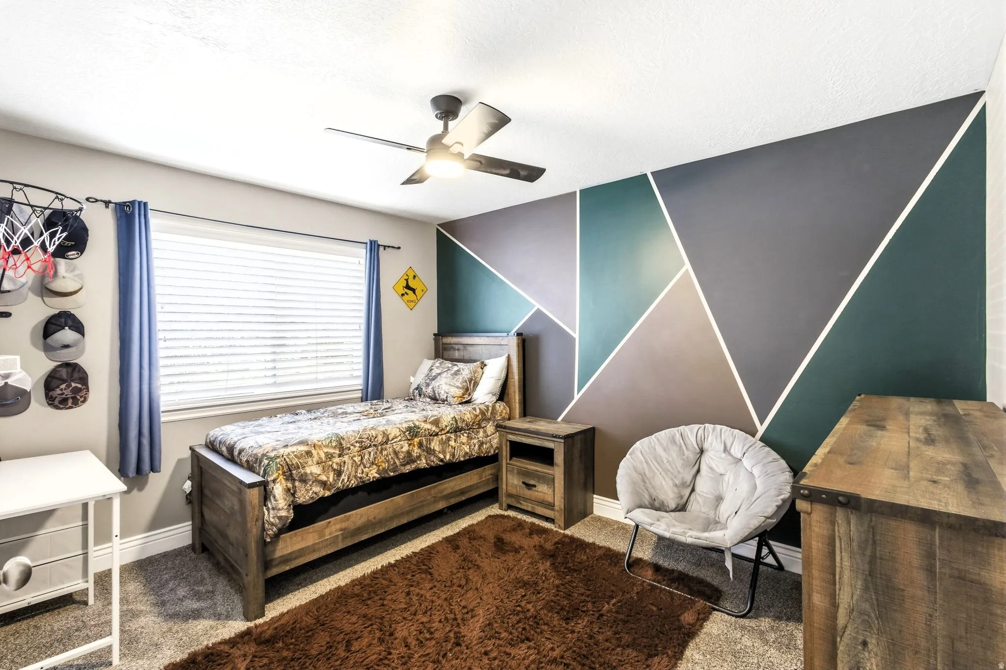 Bedroom #2 with accent wall with geometric design, ceiling fan with integrated lighting, window with blinds, wood-finish bed frame, and wood-finish nightstand