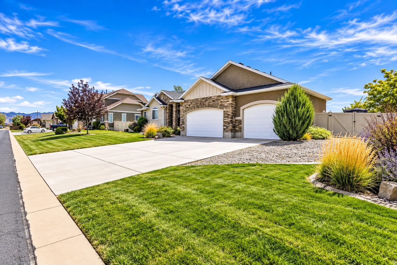 Stucco and stone facade, arched garage doors, concrete driveway, manicured lawn, and established landscaping with plenty of RV parking behind gate.