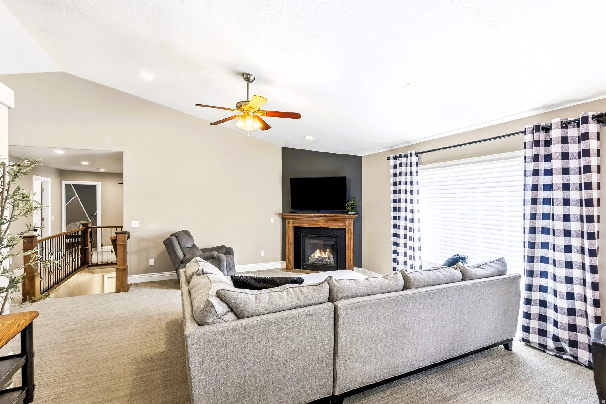 Vaulted ceiling with a ceiling fan, fireplace with a wood-finish mantel, carpet and large windows