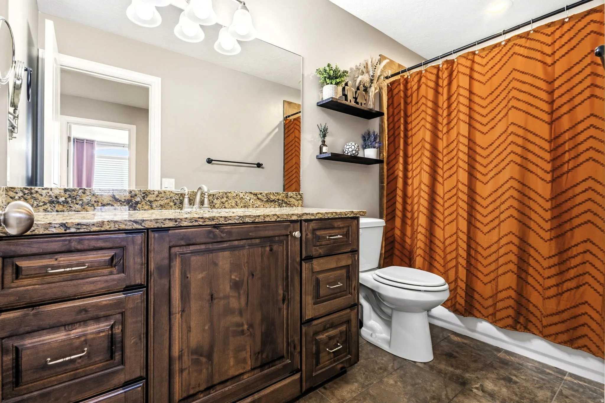 Dark wood-finish vanity with a granite countertop, large wall-mounted mirror, and tile flooring